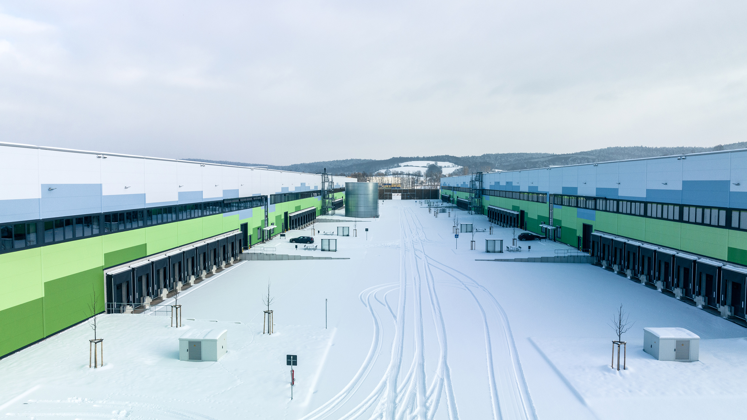 Luftaufnahme eines Industriegebiets mit farbigen Gebäuden und verschneitem Gelände. Wege im Schnee sind sichtbar.