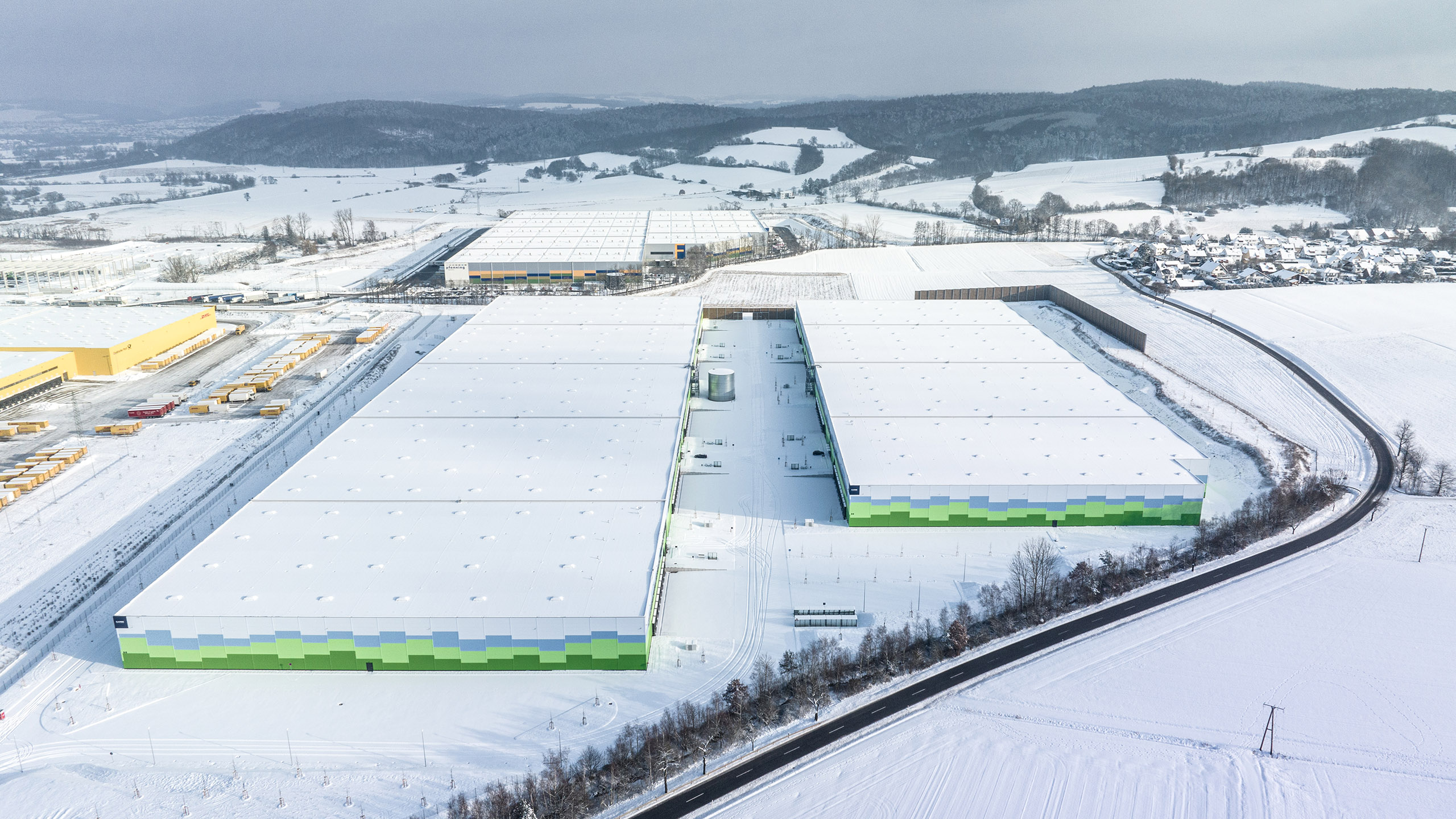 Luftaufnahme eines lagerähnlichen Gebäudekomplexes in einer schneebedeckten Landschaft.