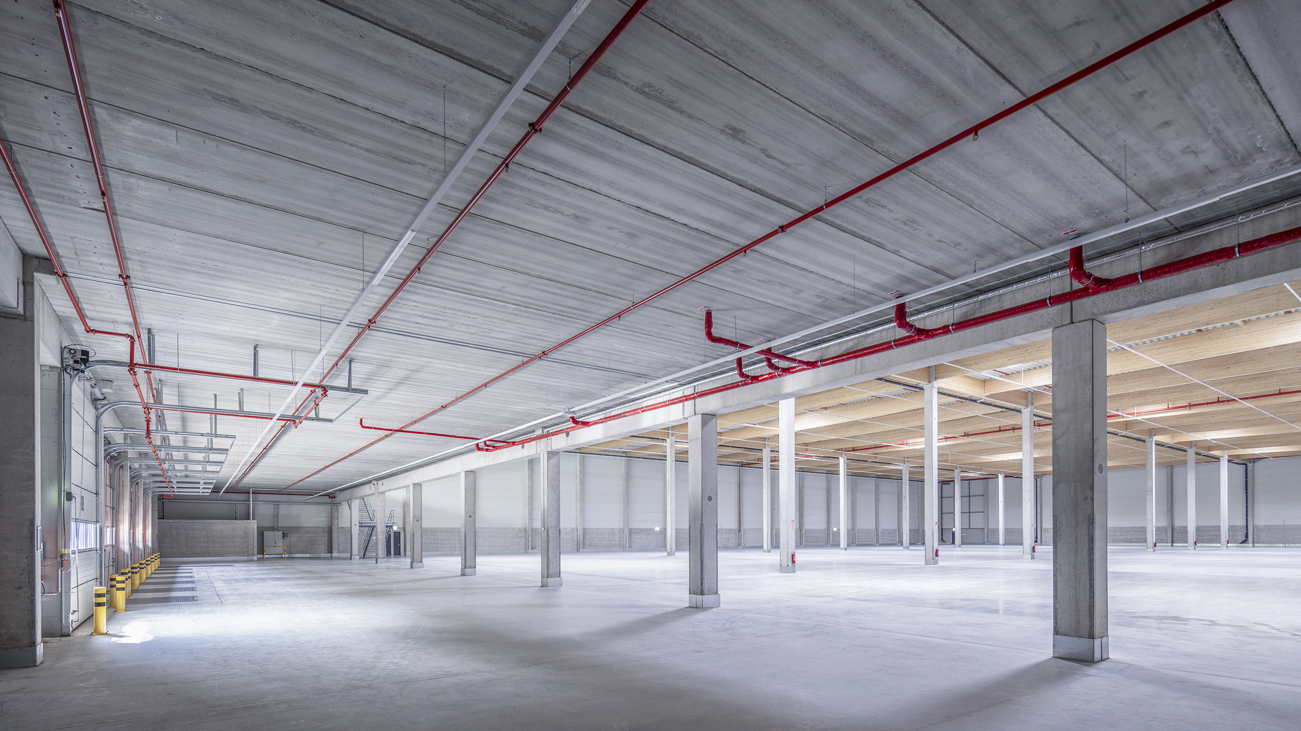 Weißer Raum mit Betonwänden, rotem Rohrleitungssystem und Säulen, geeignet für Lager oder industrielle Nutzung.