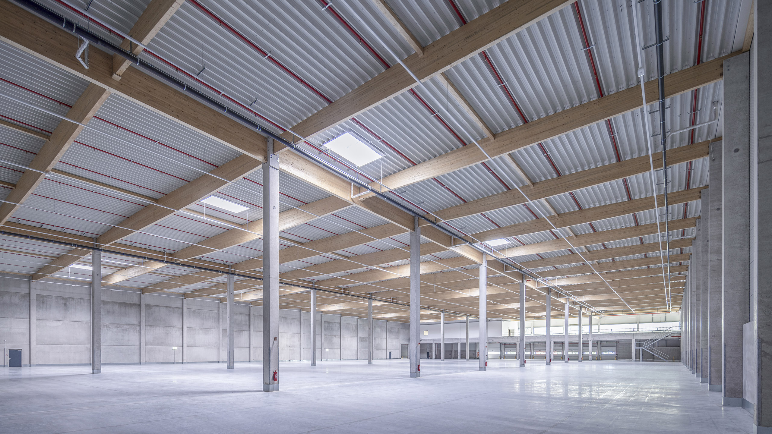 Weitläufiger Lagerraum mit hohen Decken, Holz- und Betonstrukturen, großen Fenstern und gleichmäßiger Beleuchtung.