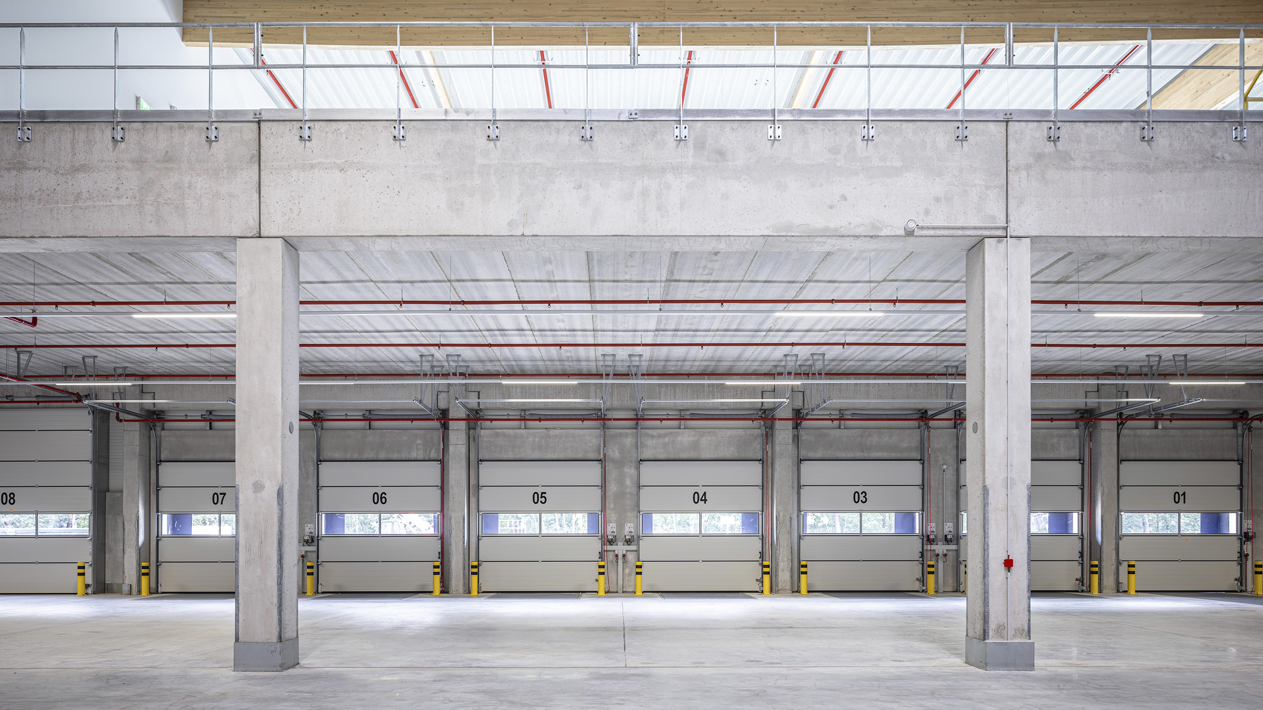 Leere Lagerhalle mit Betonstützen, mehreren Garagentoren und einer hohen Decke mit freiliegenden Rohren.