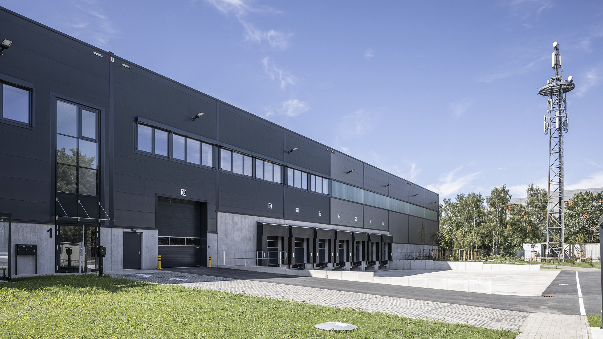 Ein modernes Lagergebäude mit Ladeflächen und Antennenmast, umgeben von einer grünen Rasenfläche und klarem Himmel.