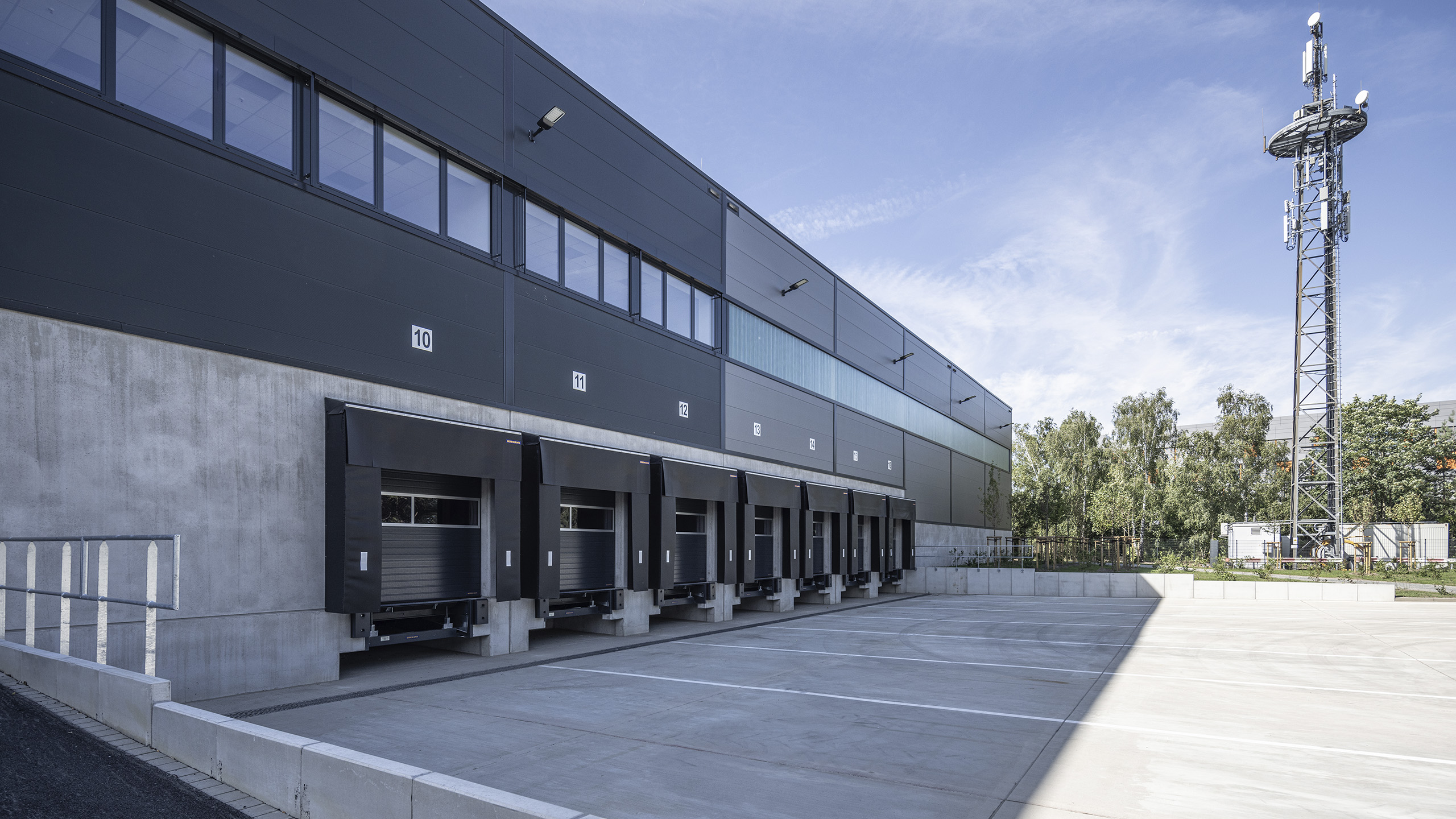 Lagerhaus mit Ladebuchten und einem Mobilfunkmast im Hintergrund an einem blauen Himmel.