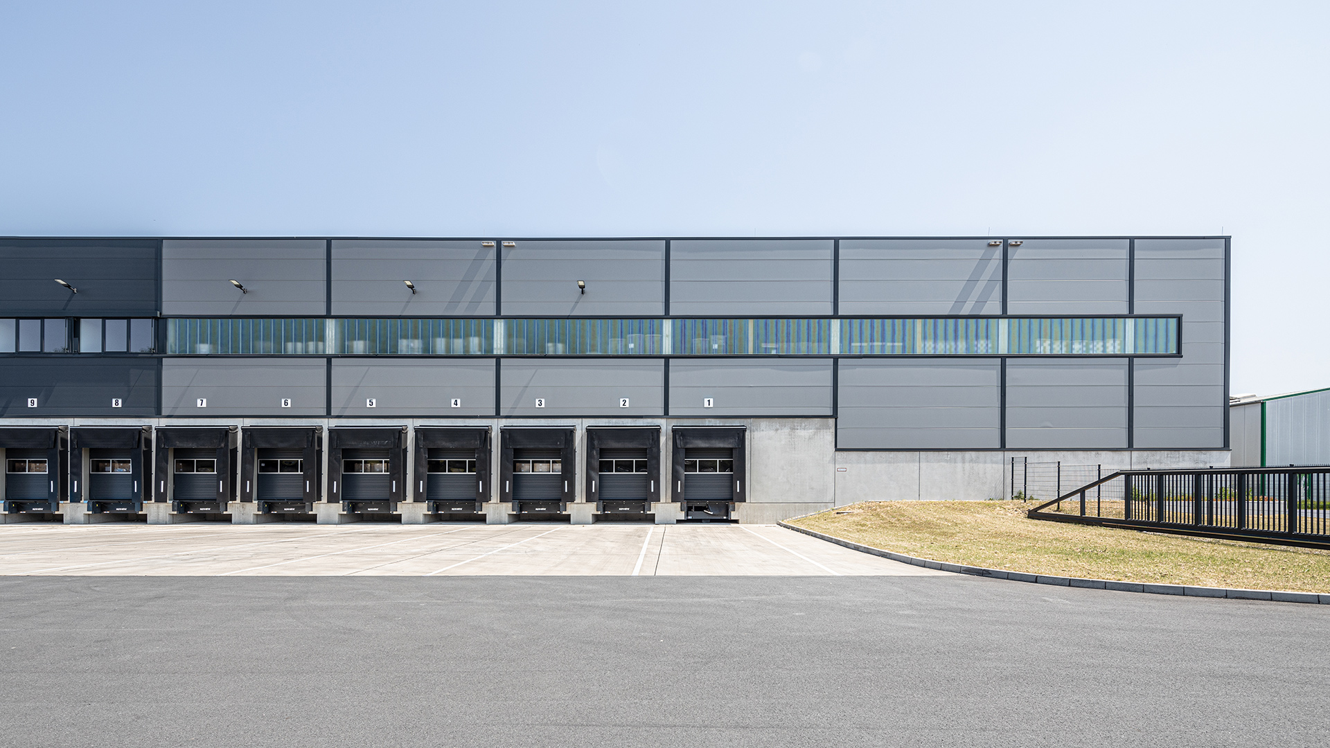 Moderne Lagerhalle mit Lkw-Rampen und großflächigen Fenstern, vor einem klaren blauen Himmel.