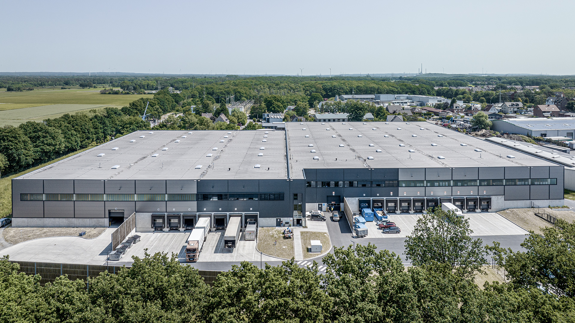 Luftaufnahme eines modernen Lagergebäudes mit Lkw-Rampen, umgeben von Bäumen und einem ländlichen Umfeld.