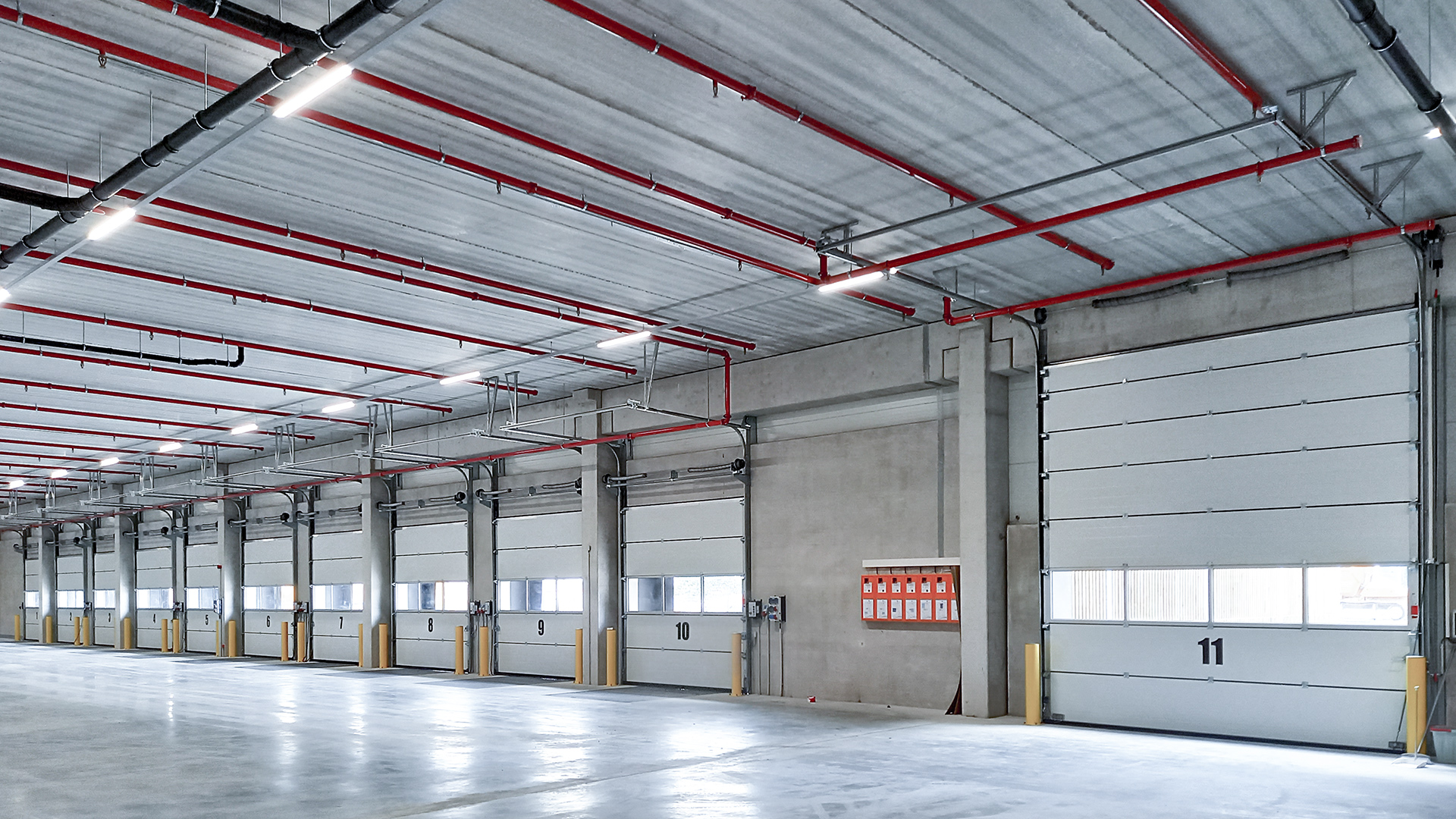 Heller, moderner Lagerraum mit mehreren Garagentoren und sichtbaren roten Rohrleitungen an der Decke.