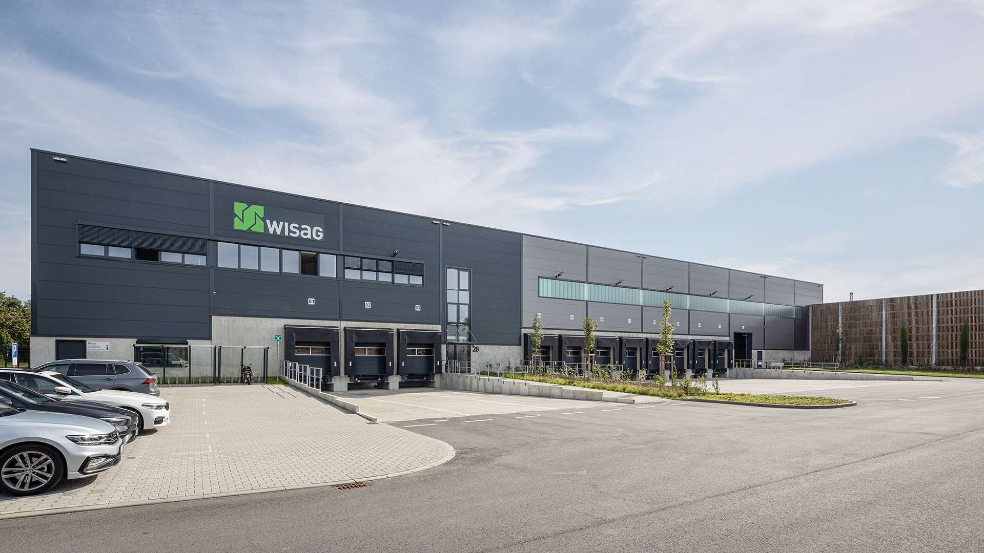 Modernes Logistikgebäude mit WISAG-Logo, Ladezonen und Parkplatz im Vordergrund, unter blauem Himmel.