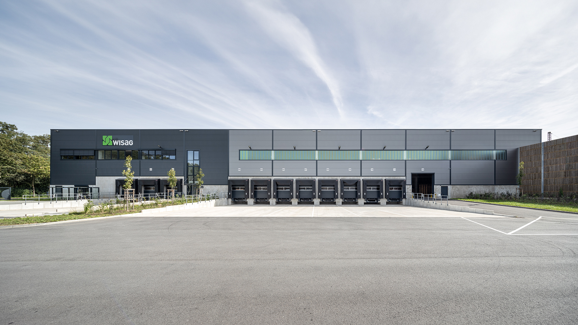 Modernes Lagergebäude mit der Aufschrift "WISAG", mehreren Ladebuchten und begrünten Flächen im Vordergrund.
