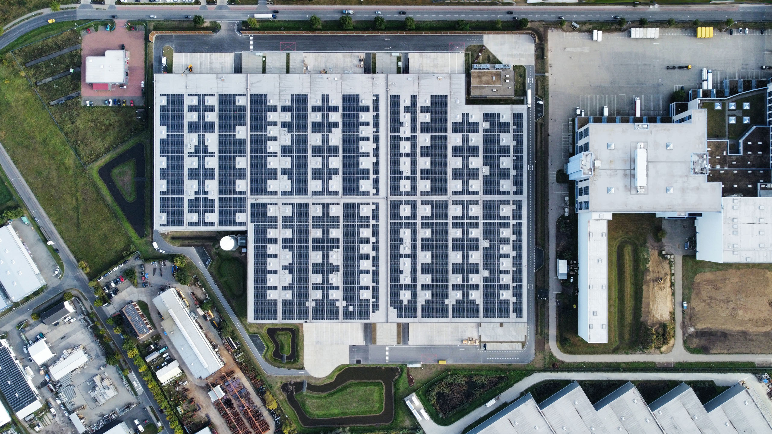 Dachansicht eines großen Gebäudes mit Solarpanelen, umgeben von weiteren Gebäuden und Grünflächen.