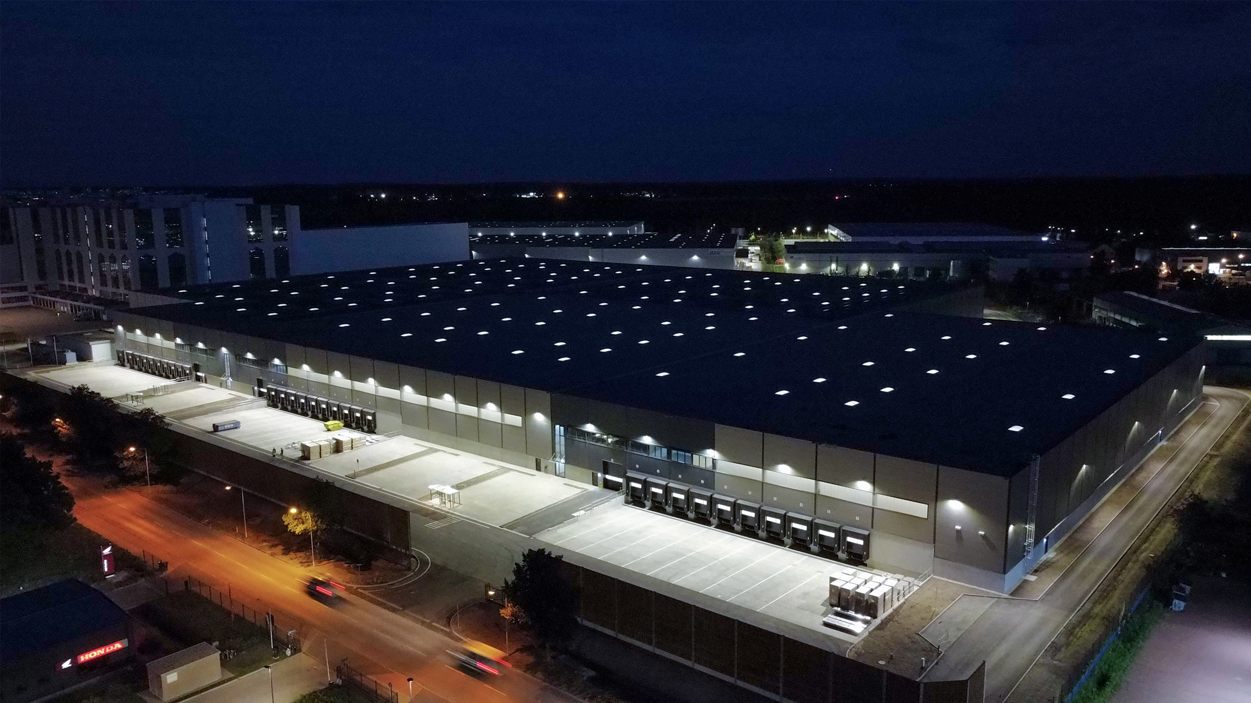 Großer Industriegebäudekomplex bei Nacht, beleuchtet mit vielen Lichtern und Ladebereichen.