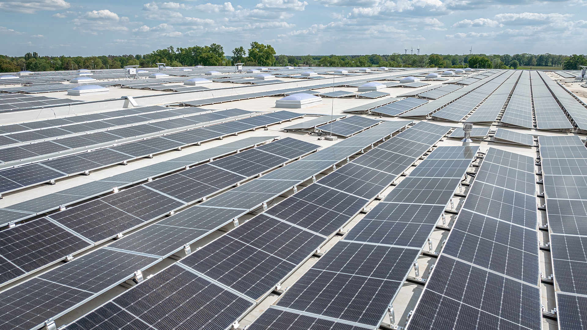 Solaranlage auf einem Dach mit PV-Modulen und Wolken am Himmel im Hintergrund.