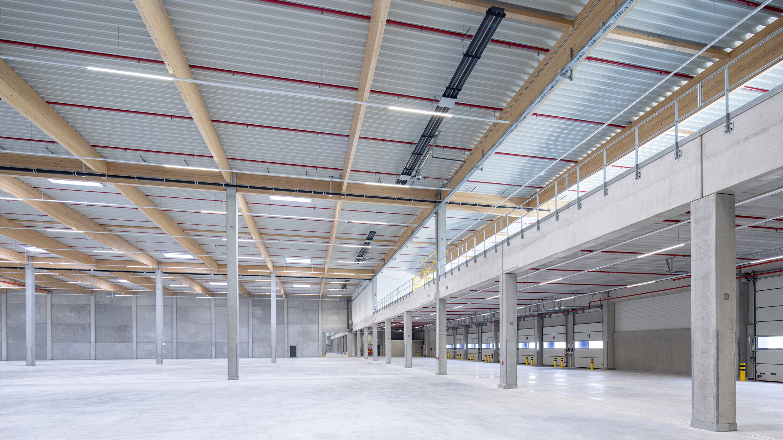 Großer, heller Lagerraum mit Holz- und Stahlkonstruktion, hoher Decke und Betonboden.