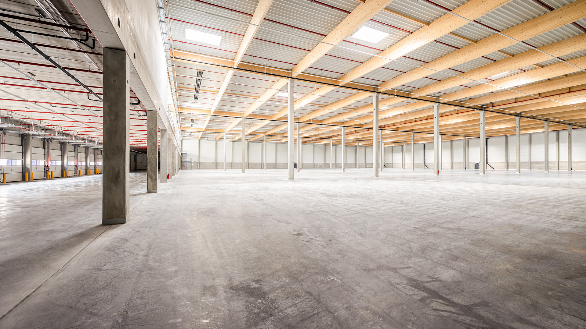 Großer leerer Innenraum mit hohen Decken und Holzträgern, Betonboden und freistehenden Säulen.