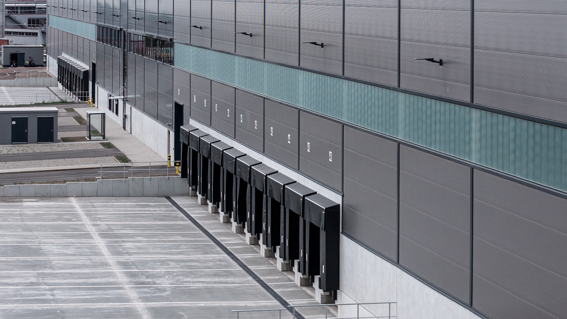 Lagergebäude mit mehreren Laderampen und Parkplatz, moderne Architektur in neutralen Farben.