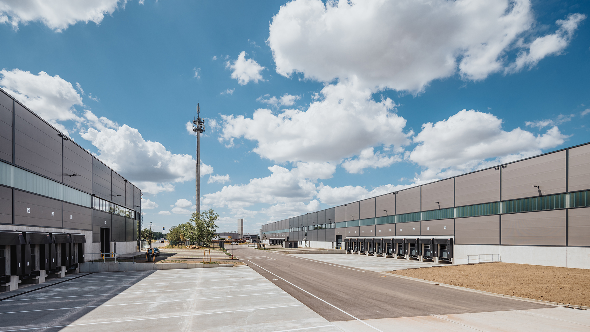 Weitläufiges Lagergelände mit Ladeplätzen, modernen Gebäuden und einer klaren blauen Himmelsszene mit Wolken.