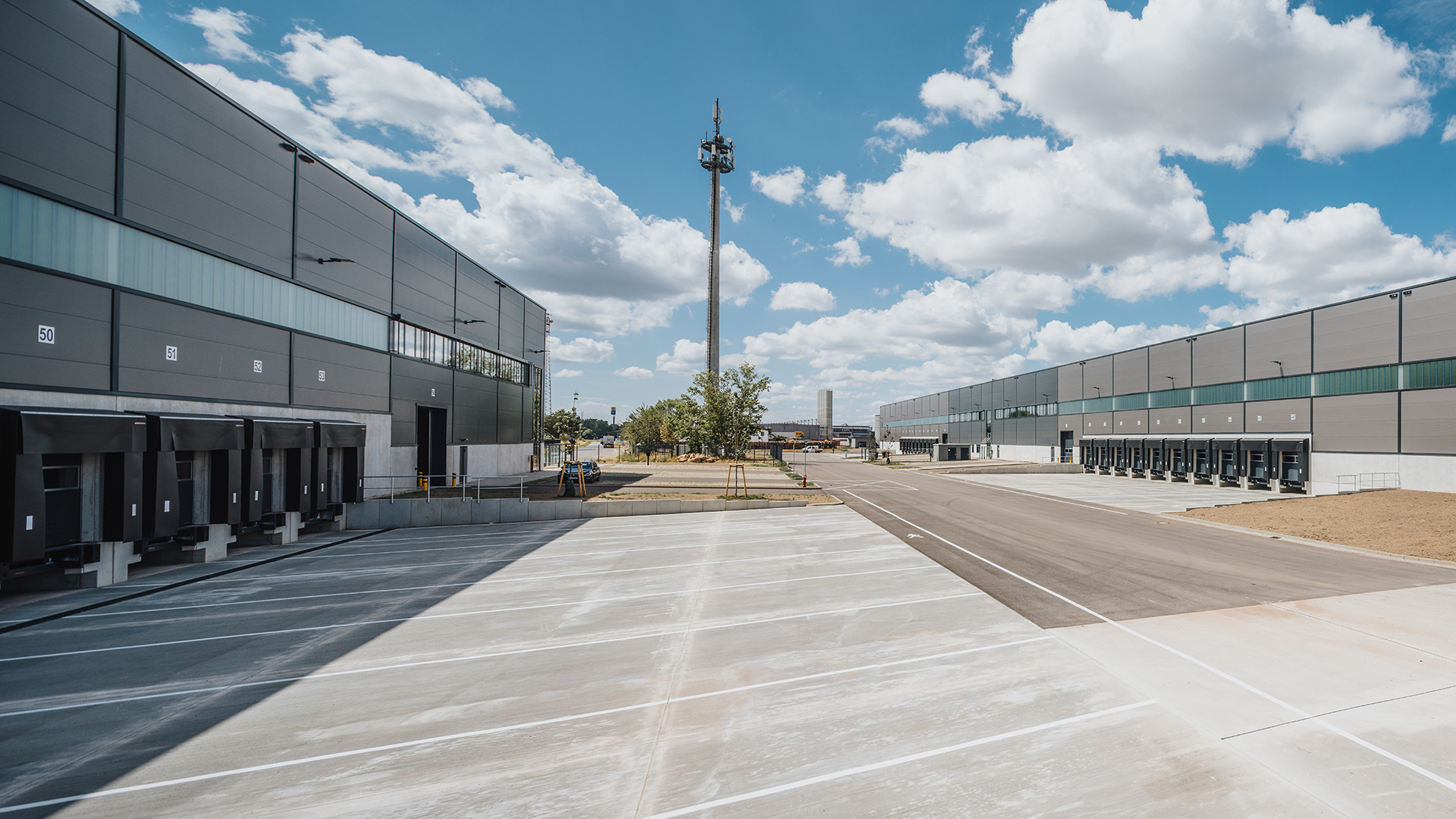 Industriegelände mit Lagerhäusern und Lkw-Entladeplätzen, unter einem klaren Himmel mit wenigen Wolken.