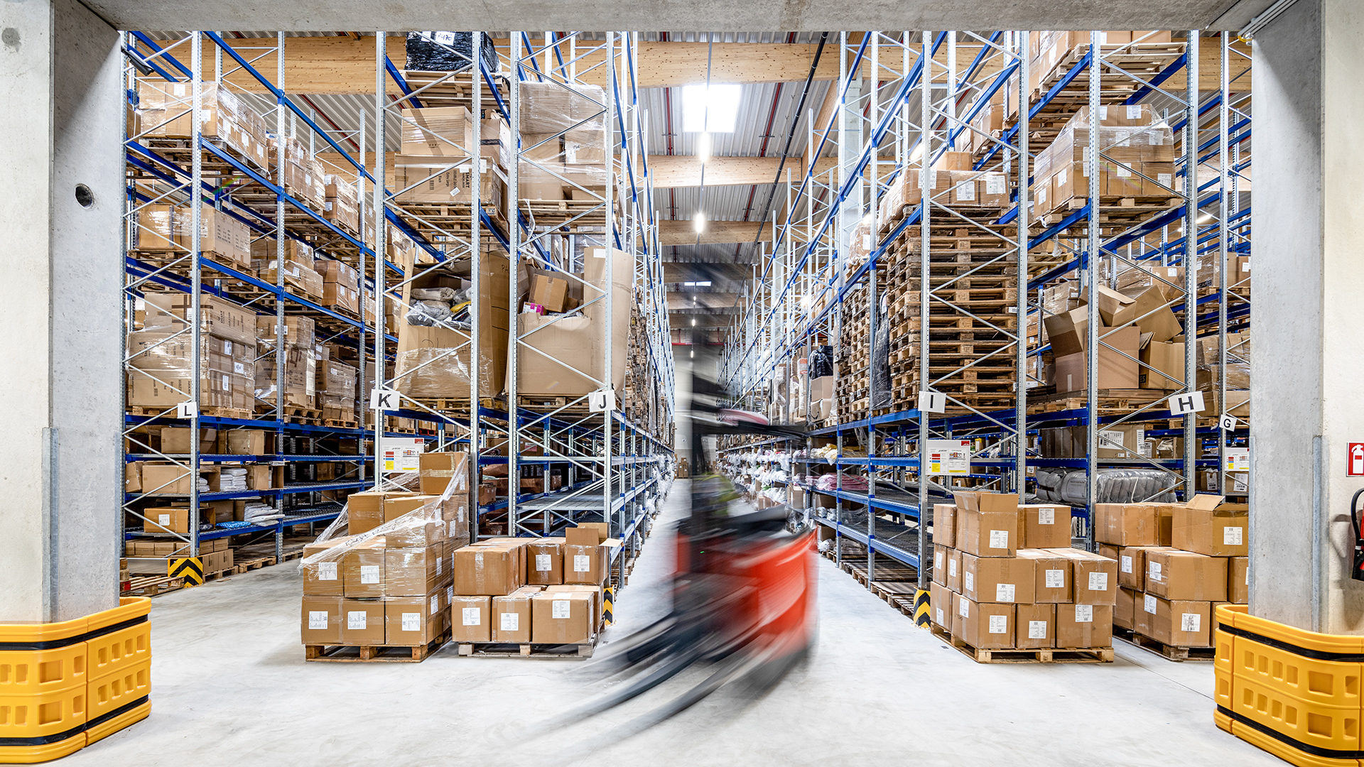 Lagerhalle mit Regalen voller Kartons und einem Gabelstapler, der durch den Gang fährt.