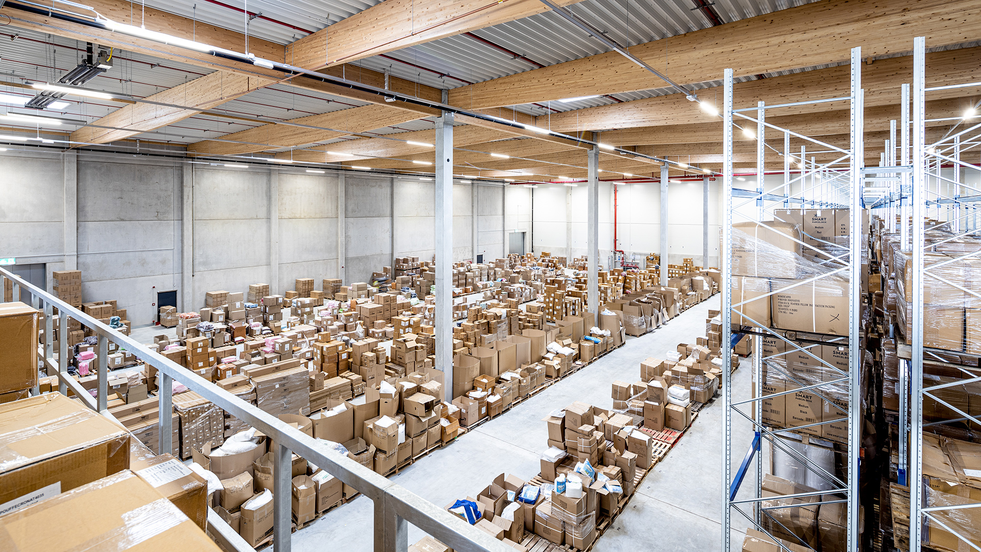 Luftaufnahme eines Lagerhauses mit vielen Kartons und Regalen, die bis zur Decke gestapelt sind. Heller, moderner Innenraum.