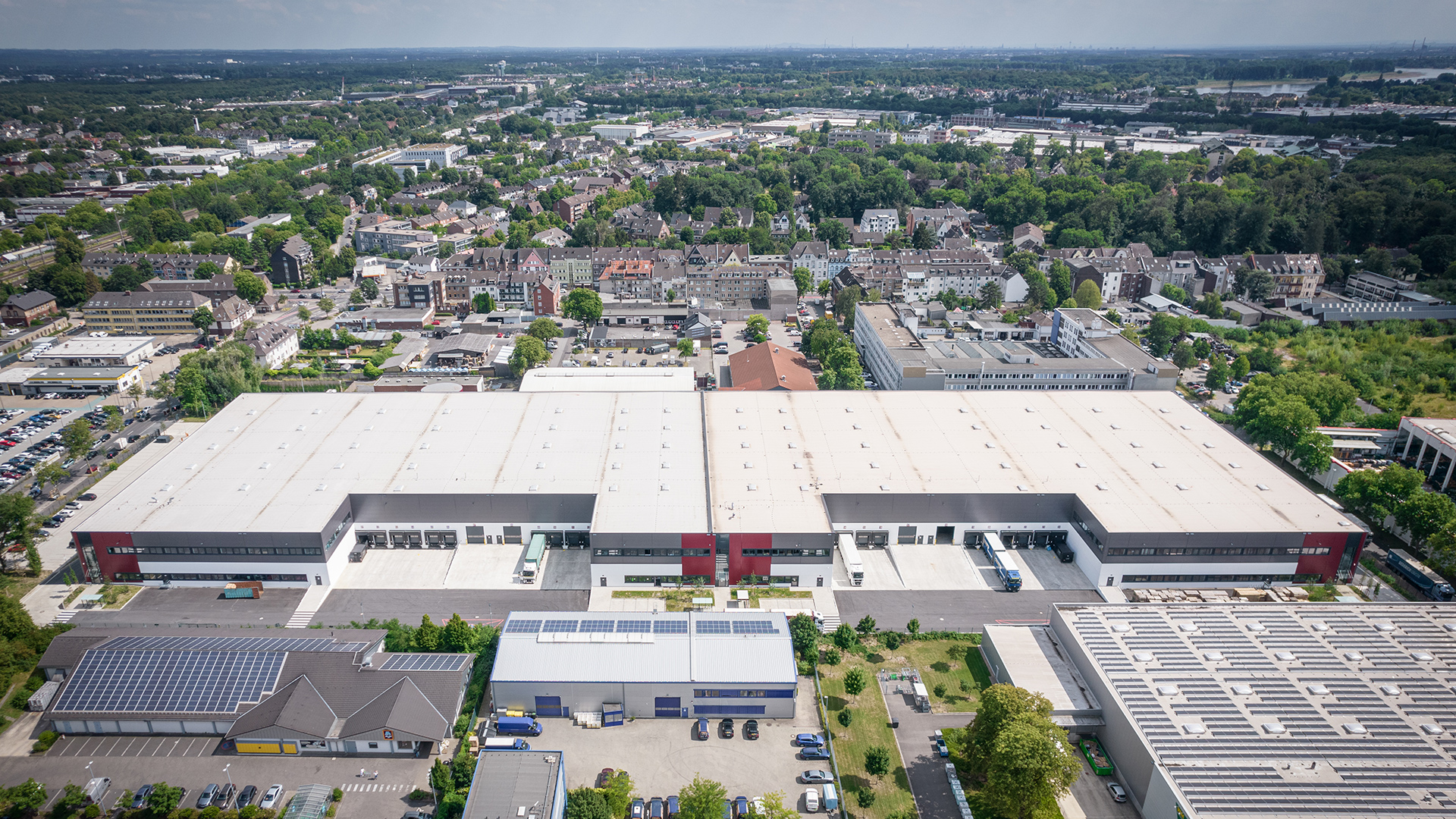 Luftaufnahme eines modernen Logistikzentrums mit umliegenden Wohngebieten und grünen Flächen.
