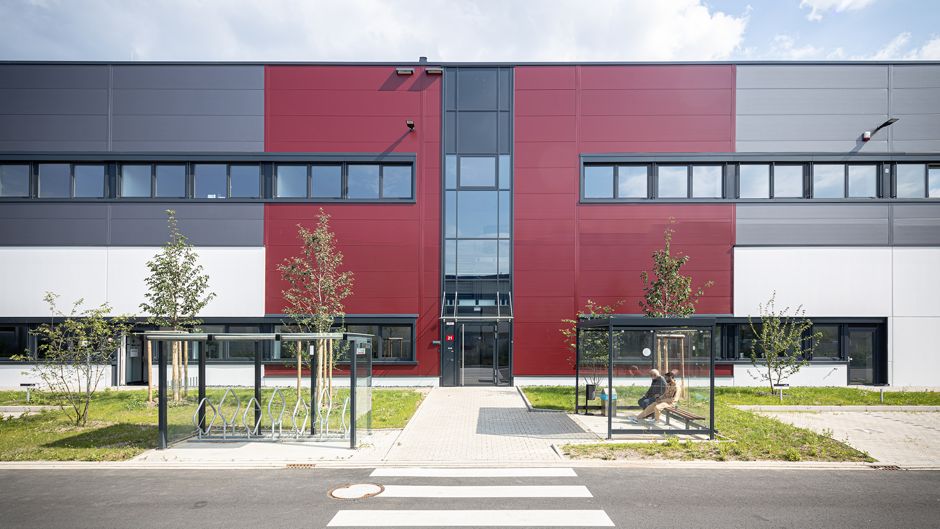 Moderne Gebäude mit farblich gestalteter Fassade, Eingangsbereich und Bushaltestelle im Vordergrund.