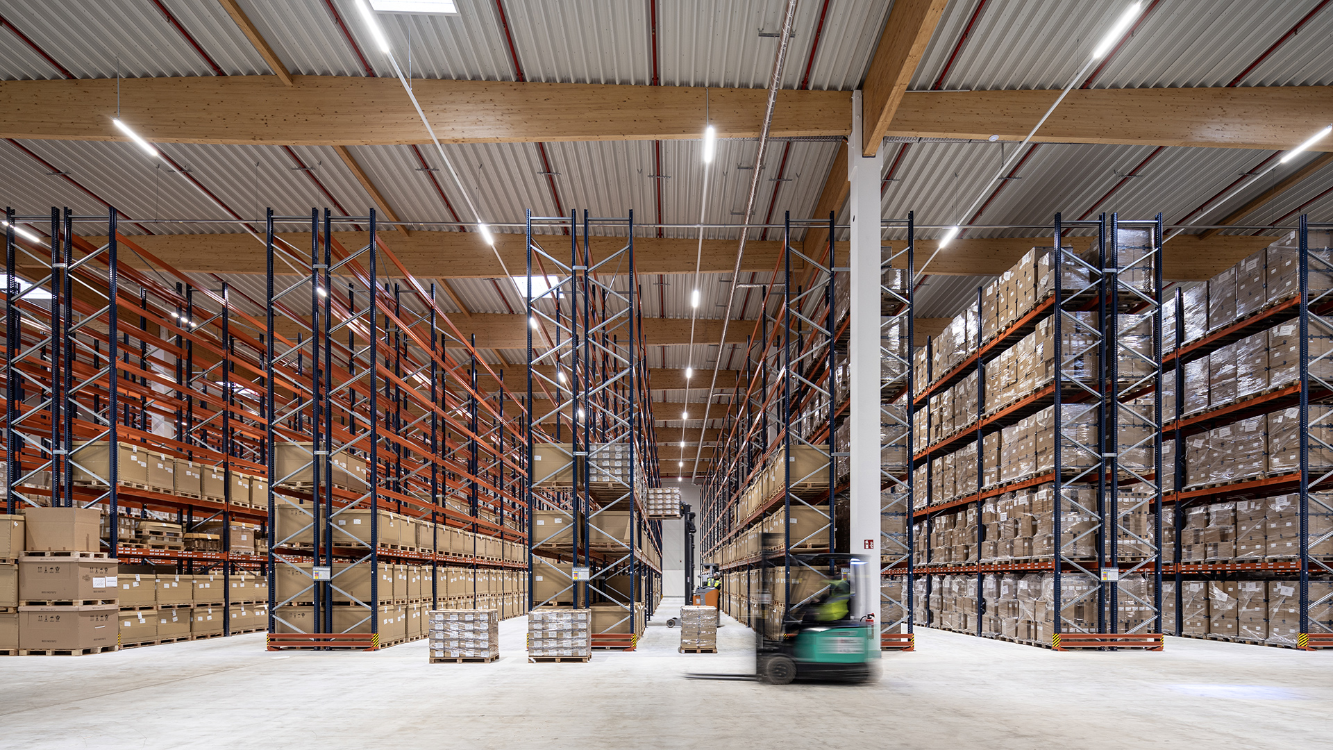 Großer Lagerraum mit hohen Regalen, gefüllt mit Kartons. Ein Gabelstapler fährt durch den Raum.