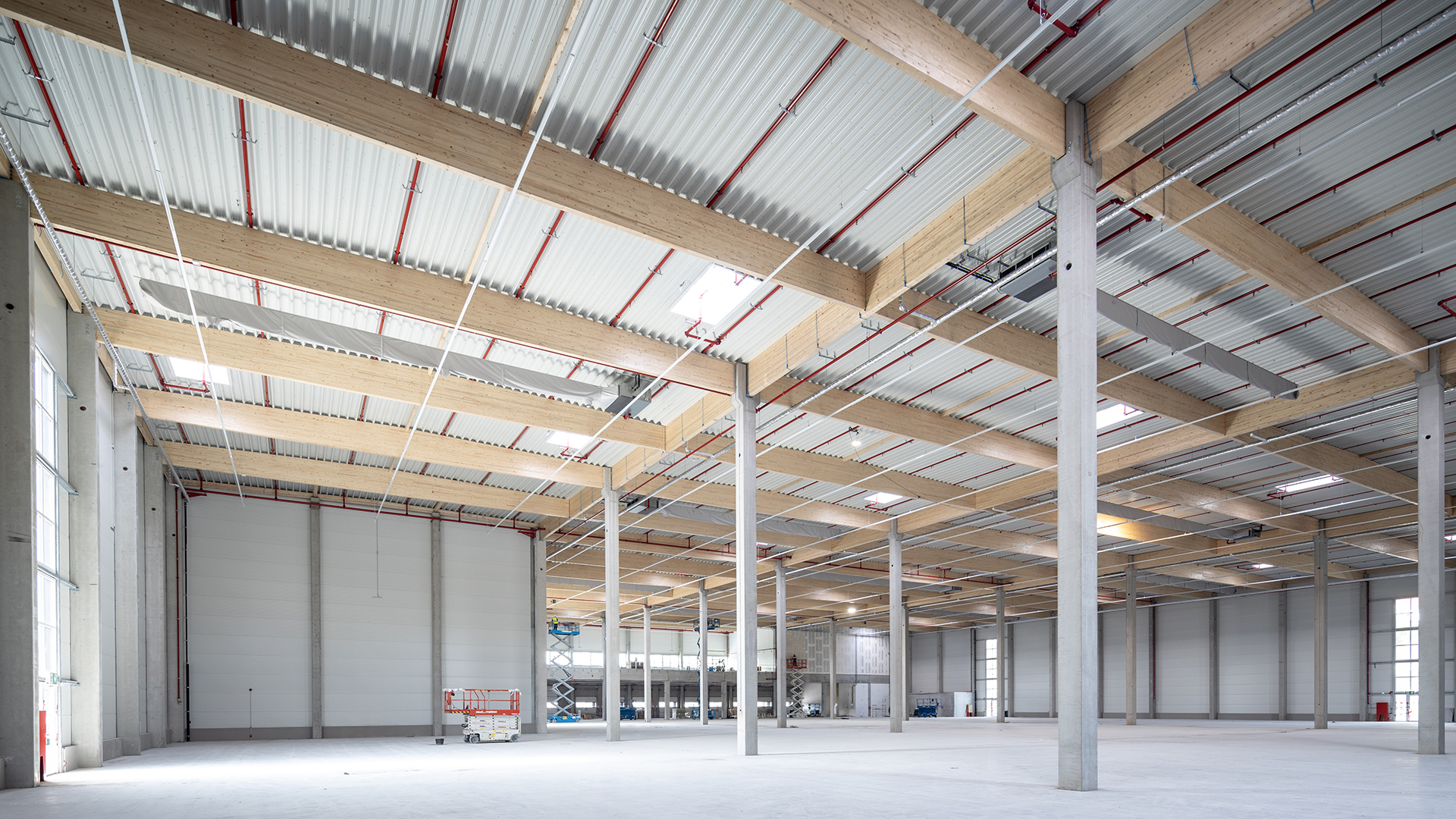 Großer, heller Innenraum mit hohen Decken, Holz- und Stahlträgern sowie sichtbaren Fensterfronten.