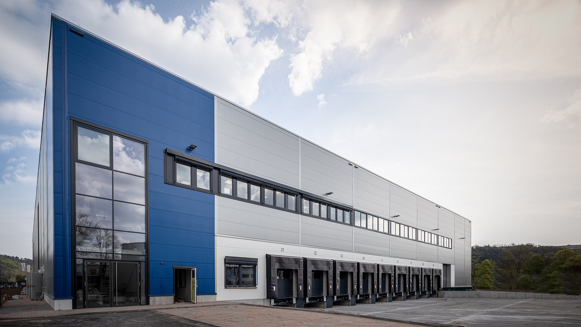 Moderner Lagergebäudekomplex mit blauer Fassade und mehreren Laderampen unter einem bewölkten Himmel.