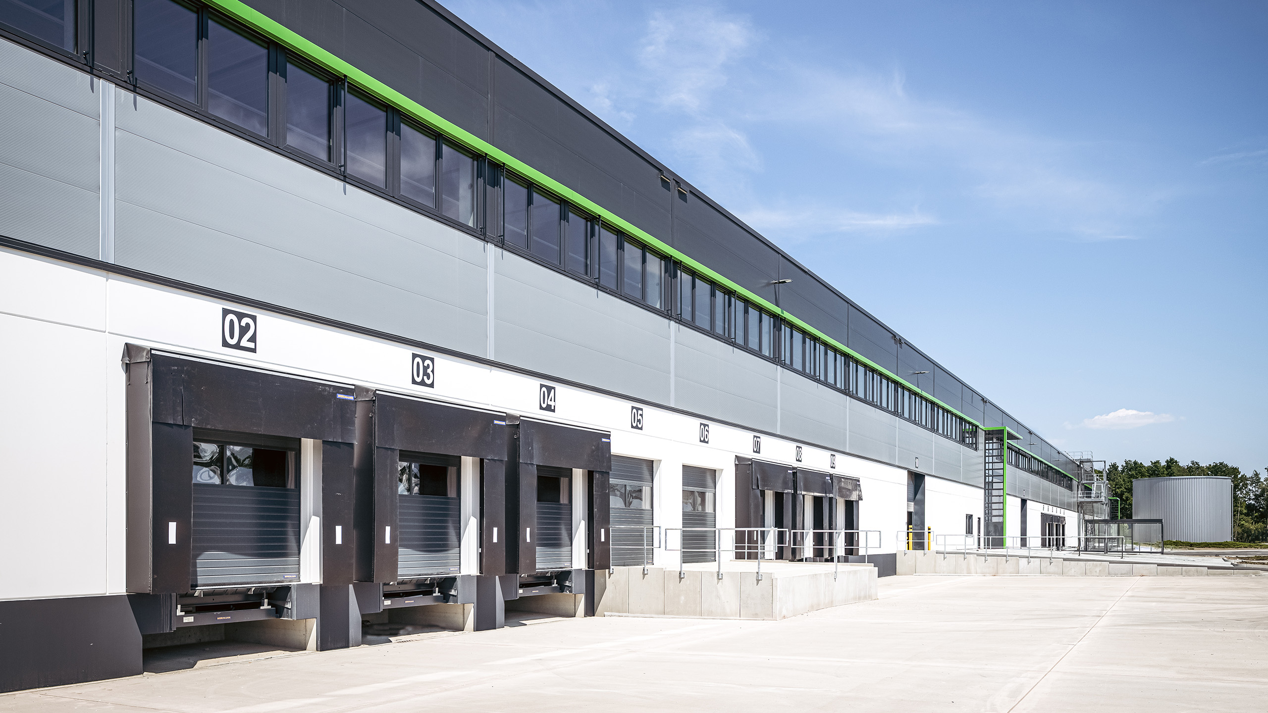 Logistikgebäude mit Verladeböden und Fensterfront unter blauen Himmel.