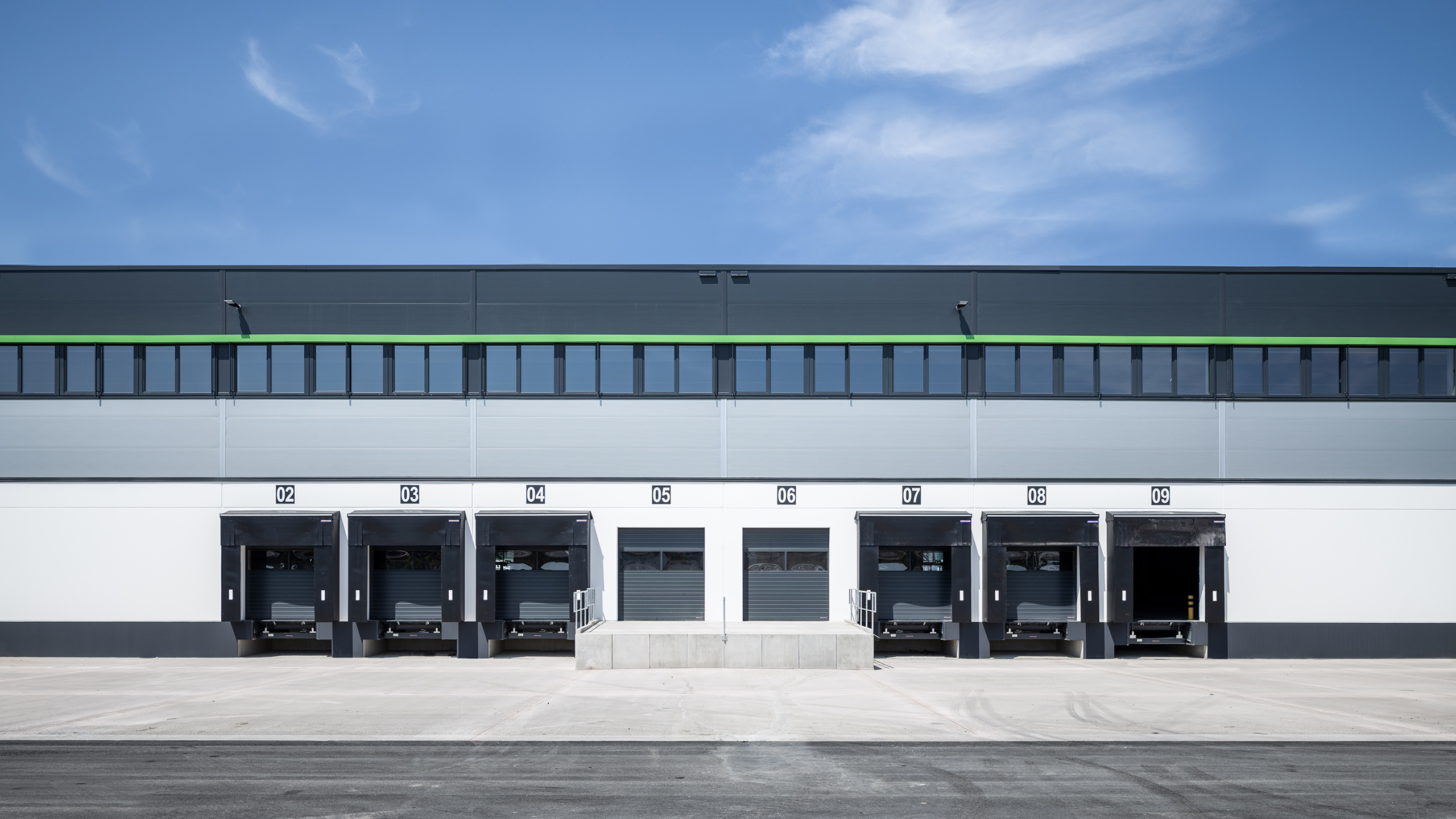 Lagerhausfassade mit mehreren Laderampen und grauem Himmel im Hintergrund, nummeriert von 02 bis 09.