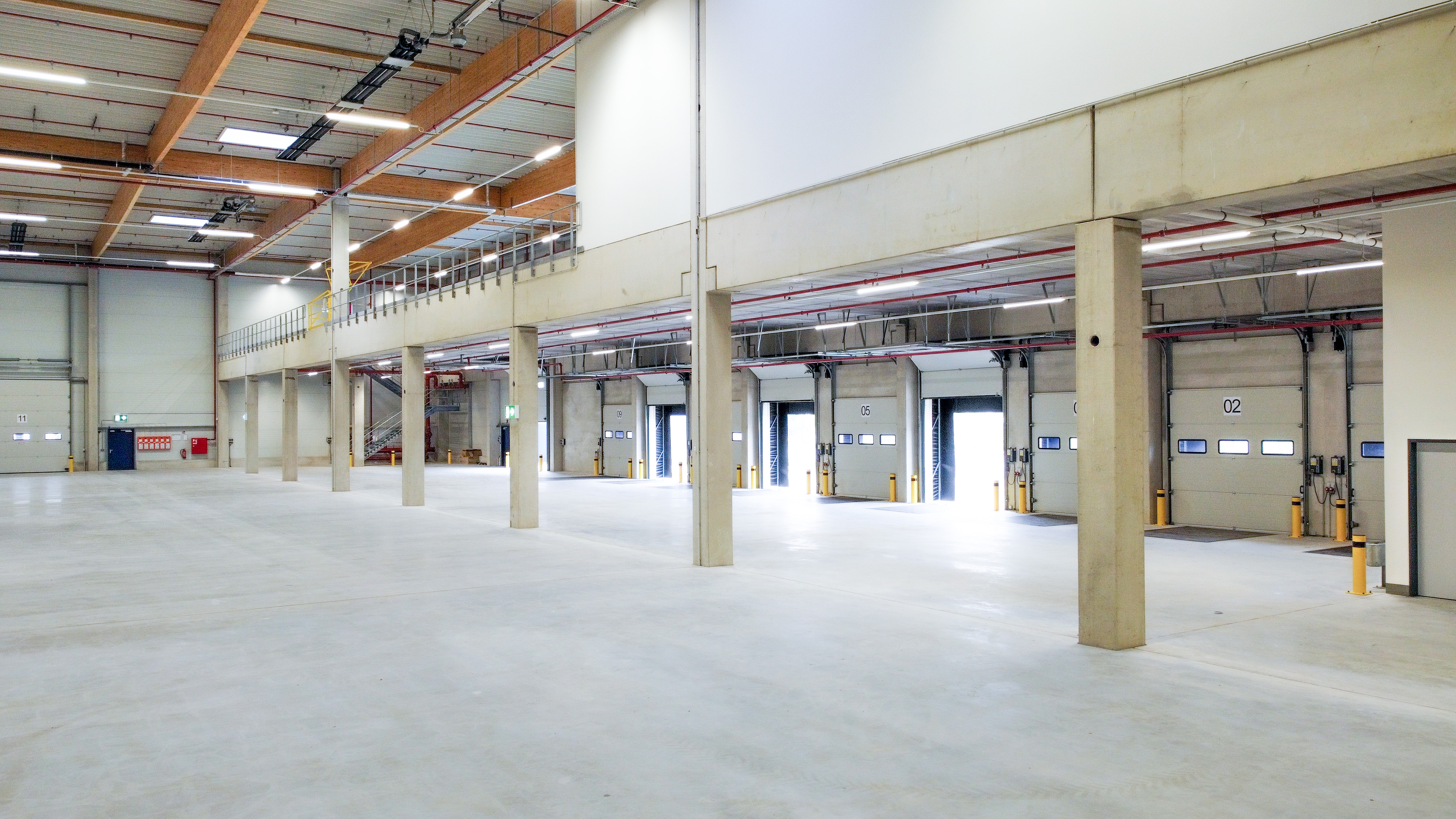Grote, leere Lagerhalle mit hohen Decken, Lichtquellen und Ladebuchten auf der linken Seite.