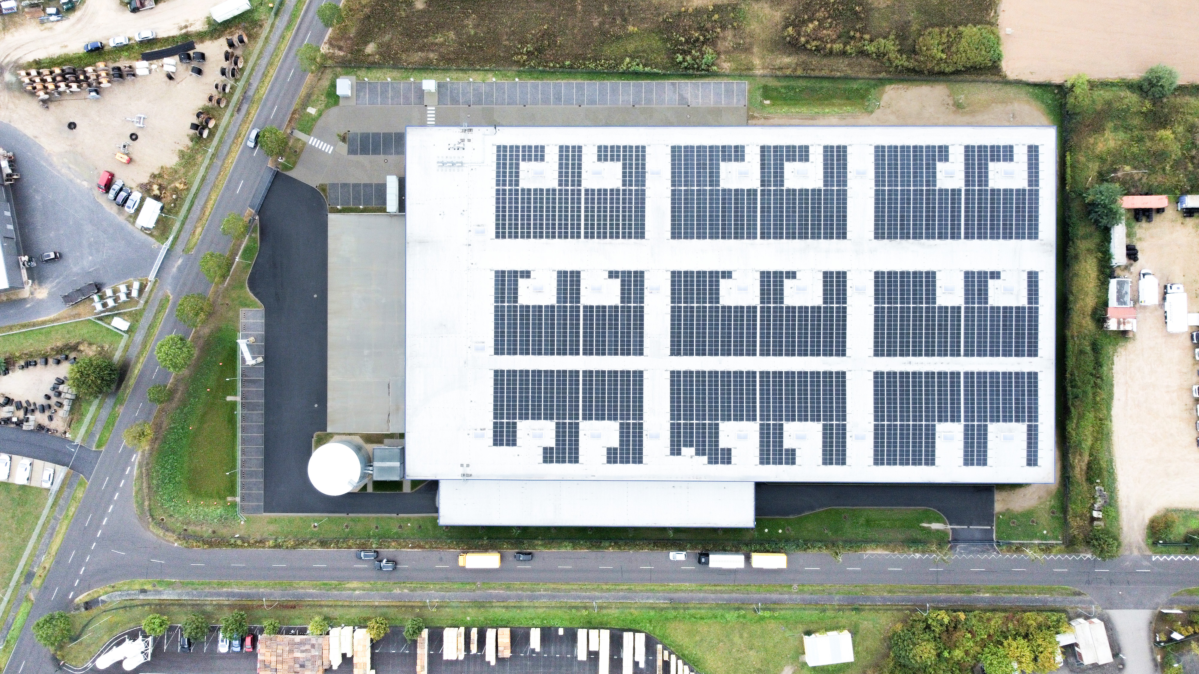 Dach eines modernen Gebäudes mit Solarpanelen, umgeben von Parkplätzen und Straßen.