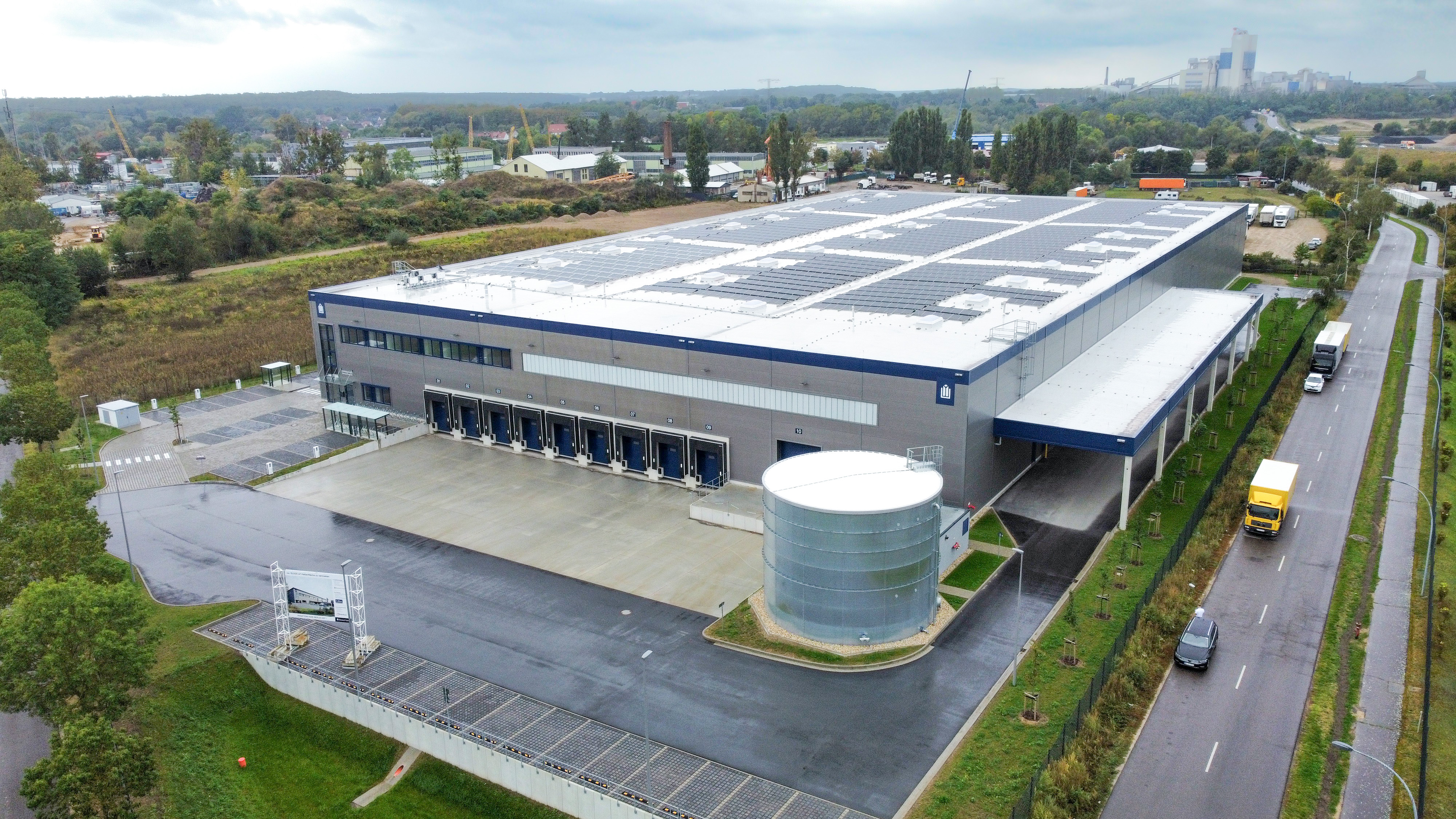 Moderne Lagerhalle mit Solarpanelen, Lkw-Laderampen und angrenzendem Parkplatz im Industriegebiet.