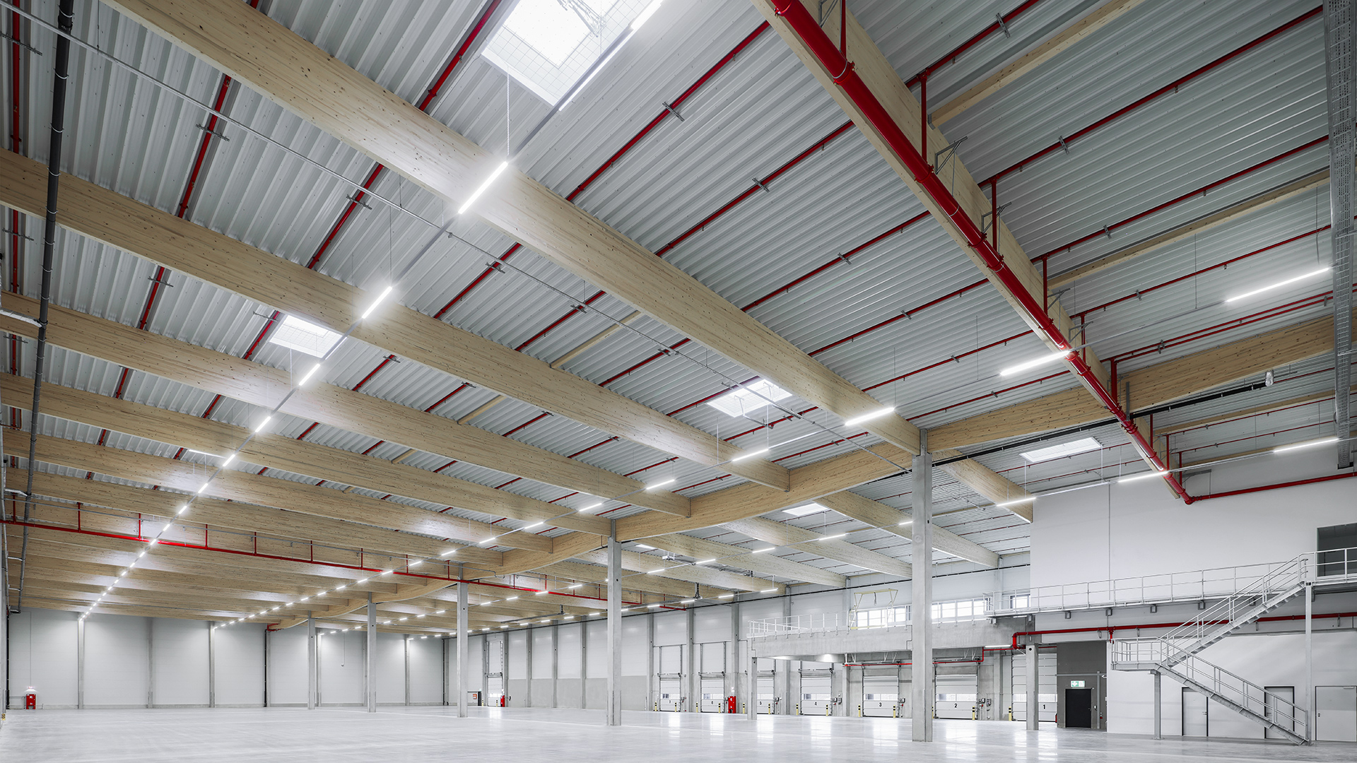 Luftaufnahme eines modernen Lagerhauses mit Holzdeckenbalken, großen Fenstern und heller Beleuchtung.