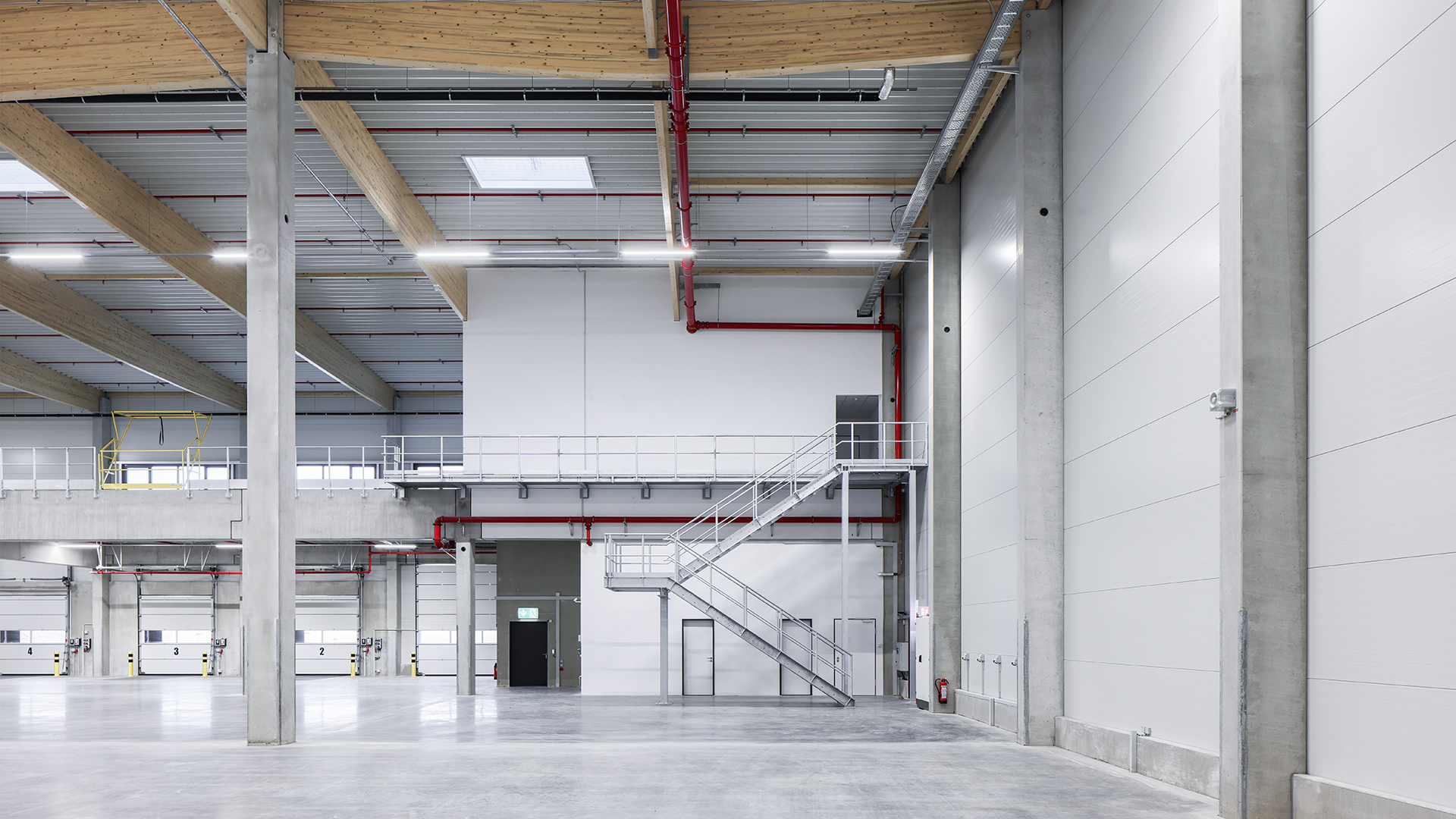 Innenansicht eines modernen, hellen Lagerhauses mit hohen Decken, Treppe und grauem Bodenbelag.
