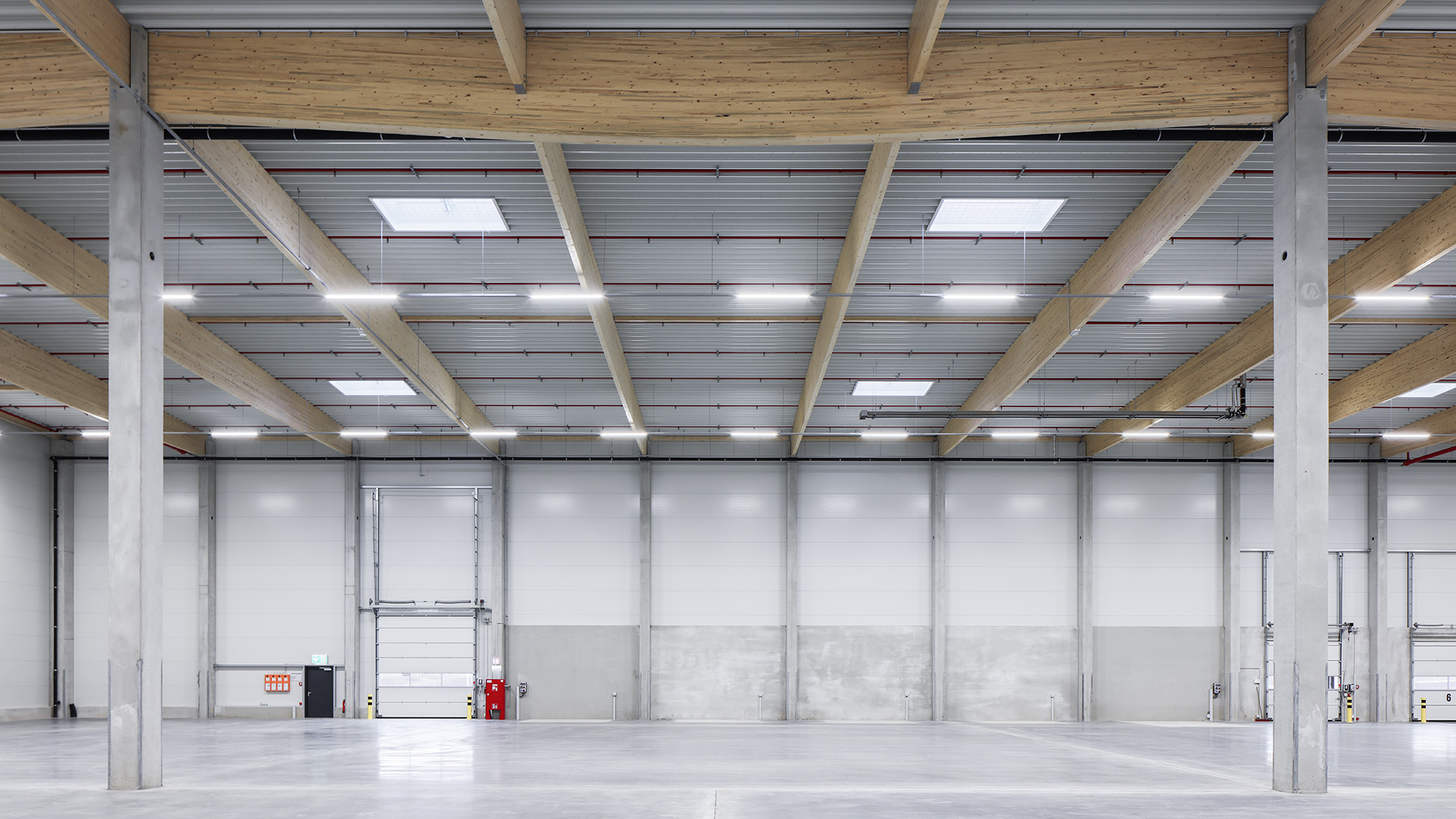 Weißer, moderner Lagerraum mit Holz- und Betondecken, beleuchtet von Deckenleuchten und Tageslicht.