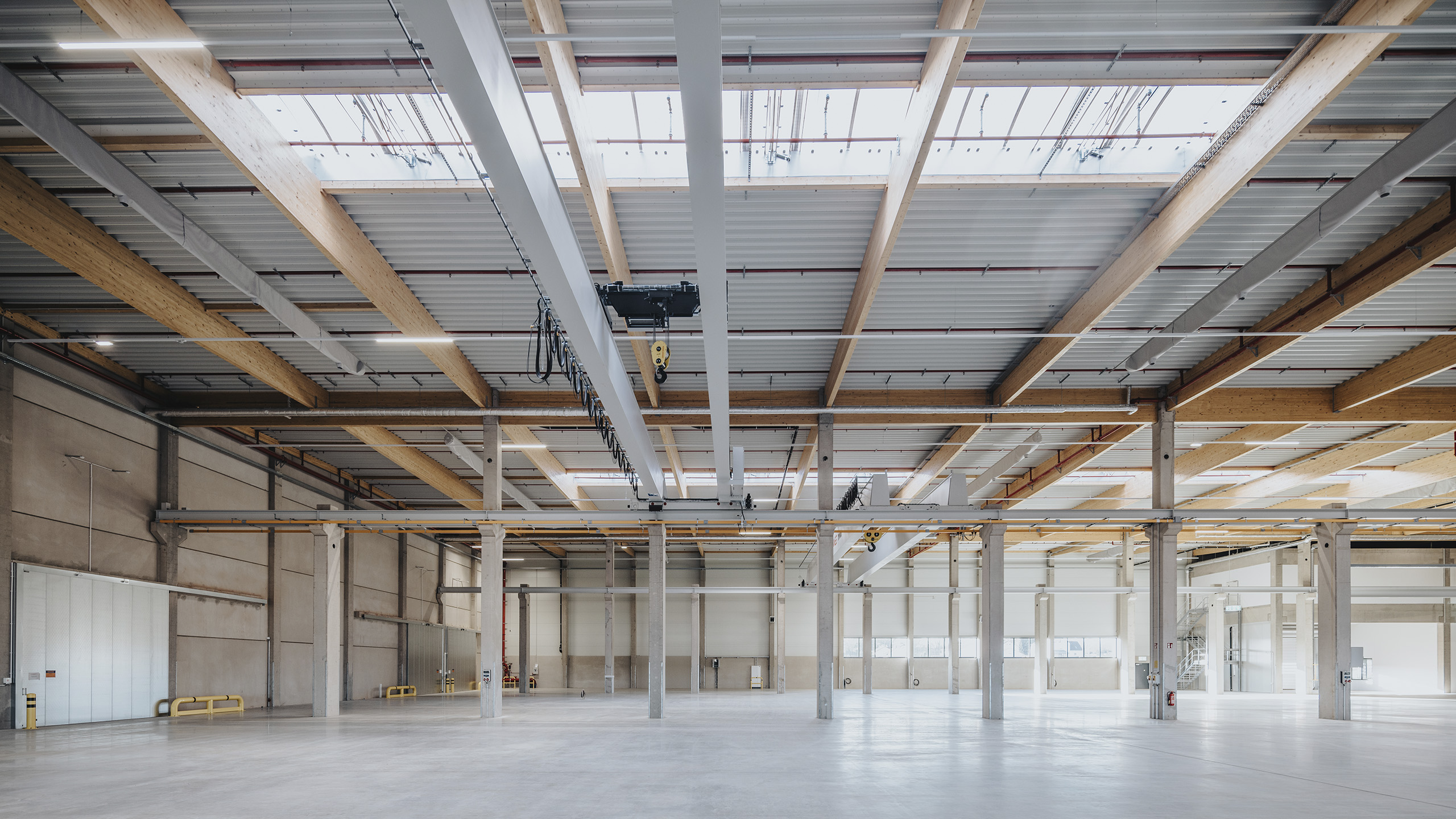 Lagerhalle mit hohen Decken, sichtbaren Holz- und Metallstrukturen sowie großen Fenstern für Tageslicht.