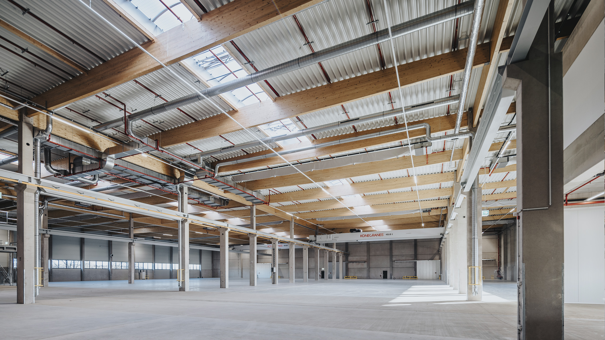 Großer Innenraum eines modernen Gewerbegebäudes mit Holzdecken und sichtbaren Rohrleitungen.