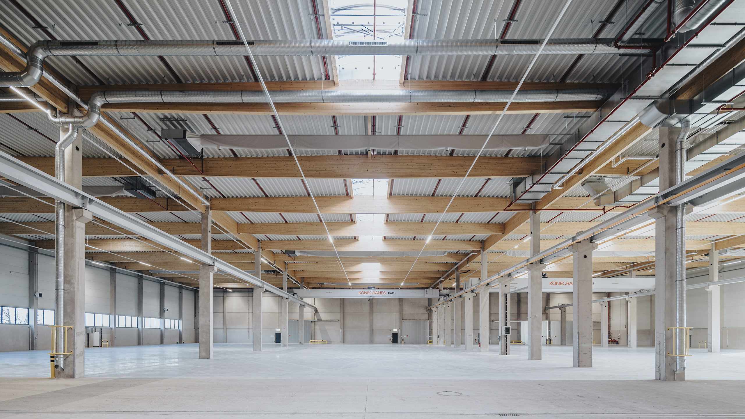 Leerer Industriehallenraum mit hohen Decken, sichtbaren Holzbalken und großen Fenstern.