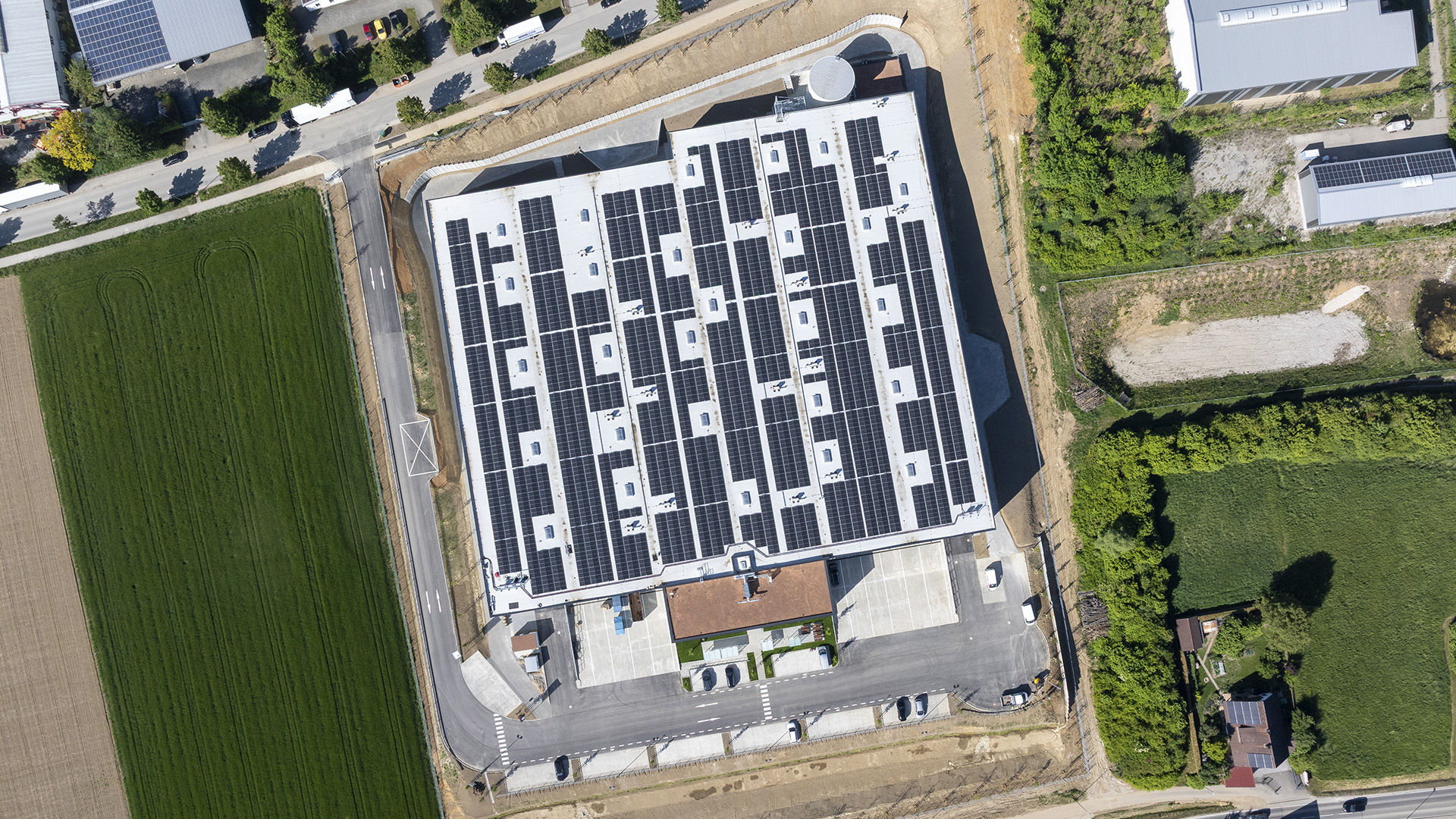 Dachansicht eines modernen Gebäudes mit Solarpanelen, umgeben von Grünflächen und Straßen.